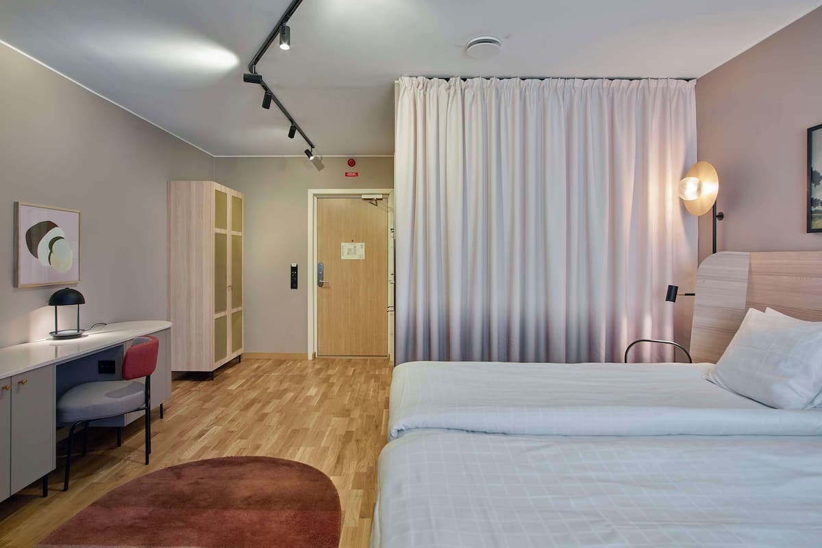 Habitación de hotel con cama, escritorio, silla, armario y una puerta que da a otra habitación.