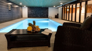 Una piscina interior con un sofá de mimbre oscuro y una mesa con fruta.