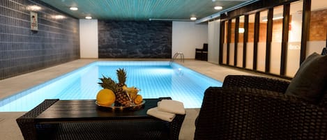 Una piscina interior con un sofá de mimbre oscuro y una mesa con fruta.