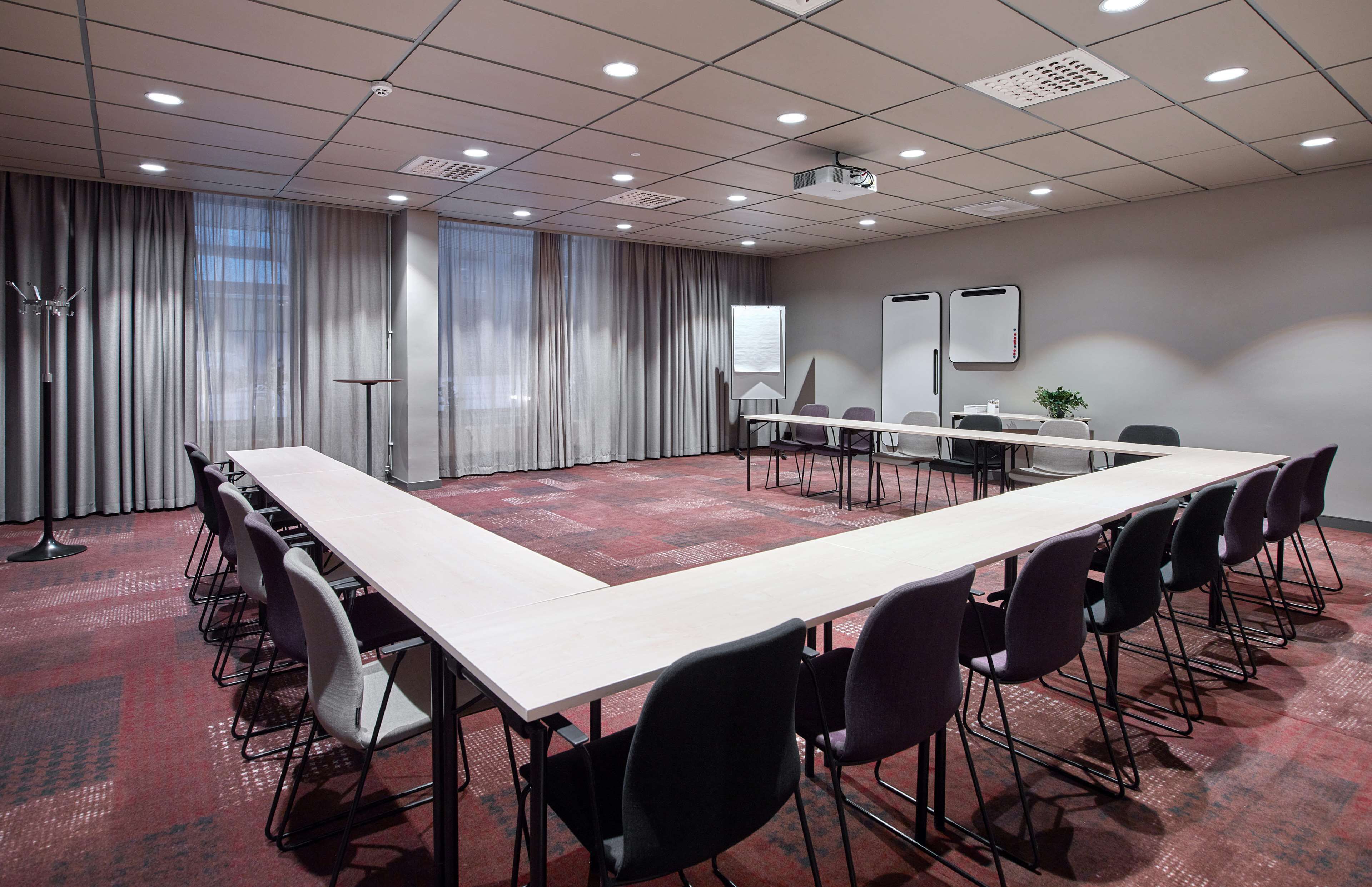 Uma sala de conferências com uma mesa comprida, cadeiras, um quadro branco e um projetor.