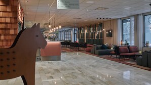 Un moderno vestíbulo de hotel con una escultura de caballo de madera, suelos de mármol y zonas de estar.