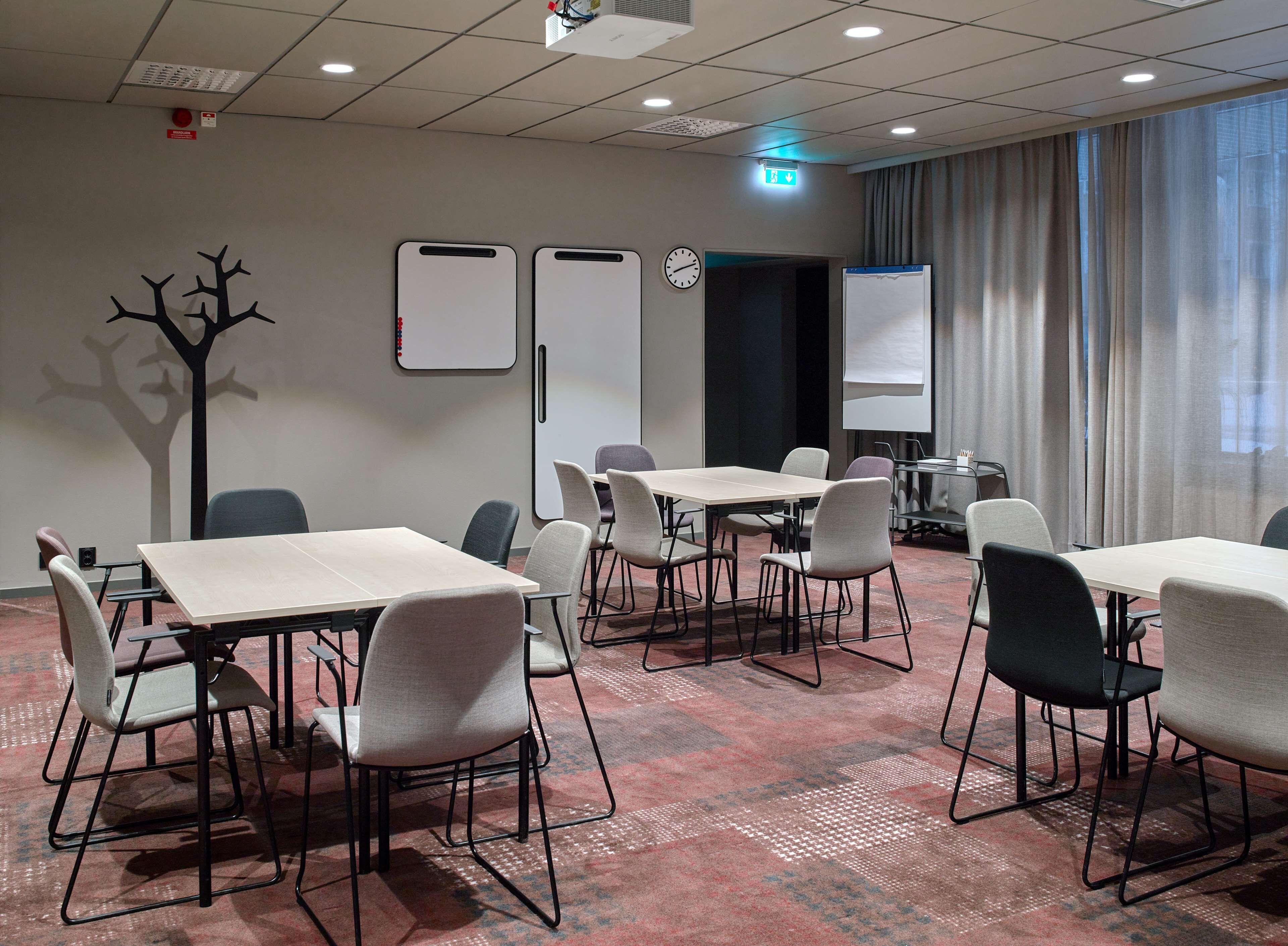 A conference room with tables and chairs, a whiteboard, a clock, and a projector screen.
