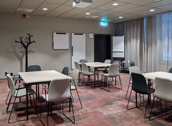 A conference room with tables and chairs, a whiteboard, a clock, and a projector screen.