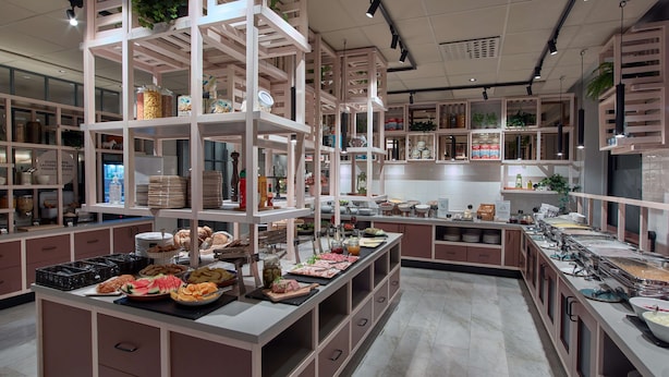 Un área de bufé bien organizada con múltiples estaciones de servicio, estantes con alimentos y un diseño interior moderno y limpio.