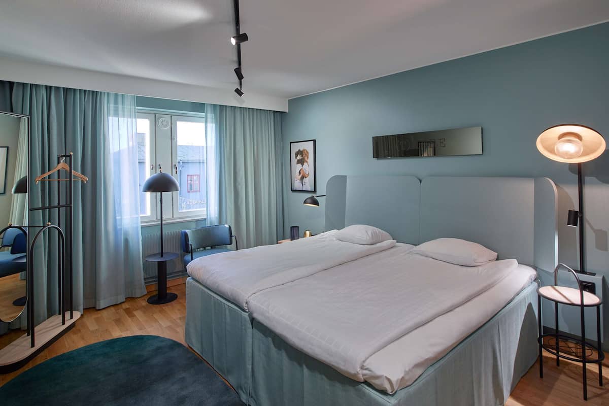 Una habitación de hotel con una cama grande, un escritorio, una silla, un armario y un espejo.
