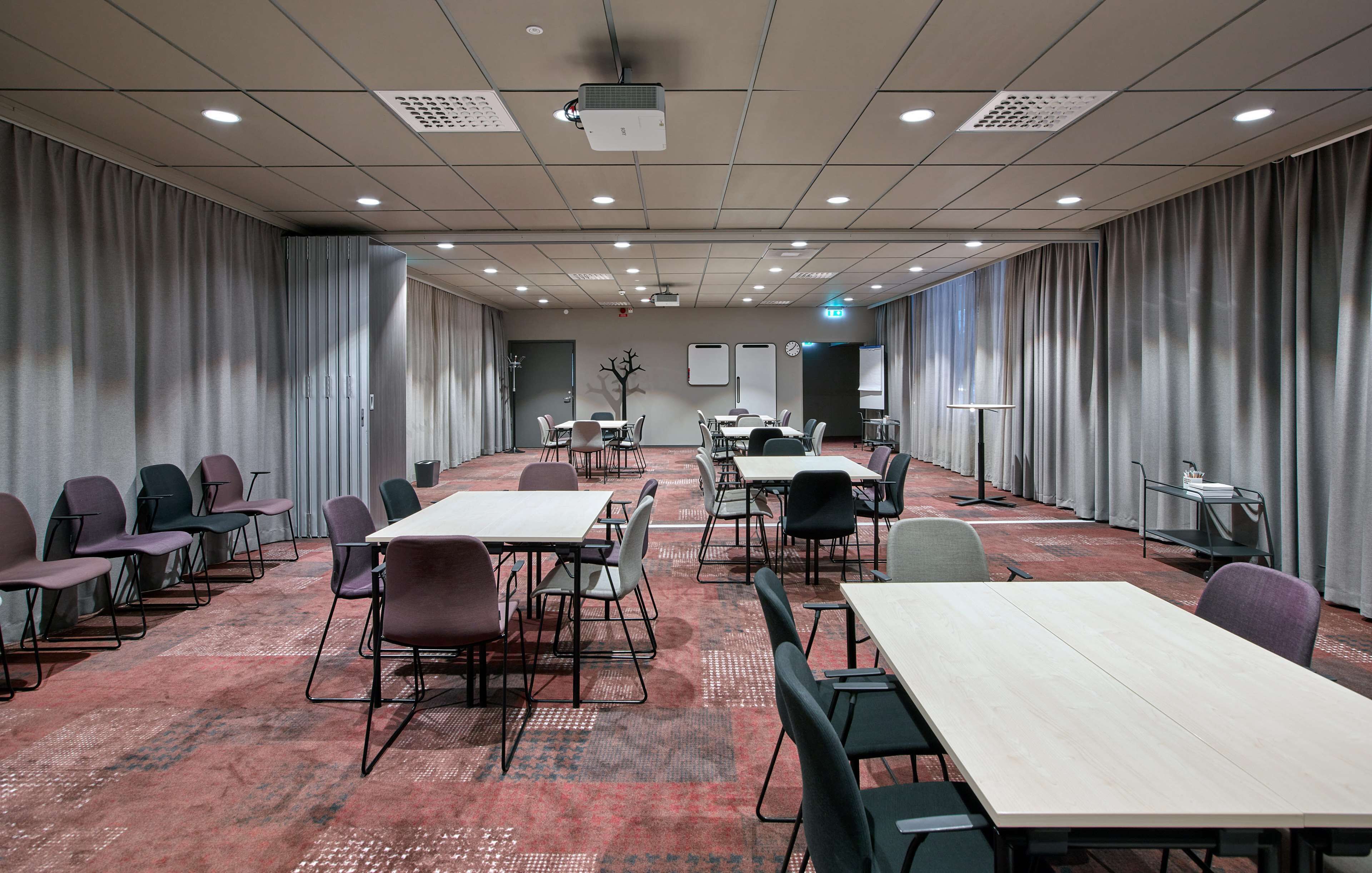 Ett konferensrum med bord och stolar, en projektor och gardiner på väggarna.
