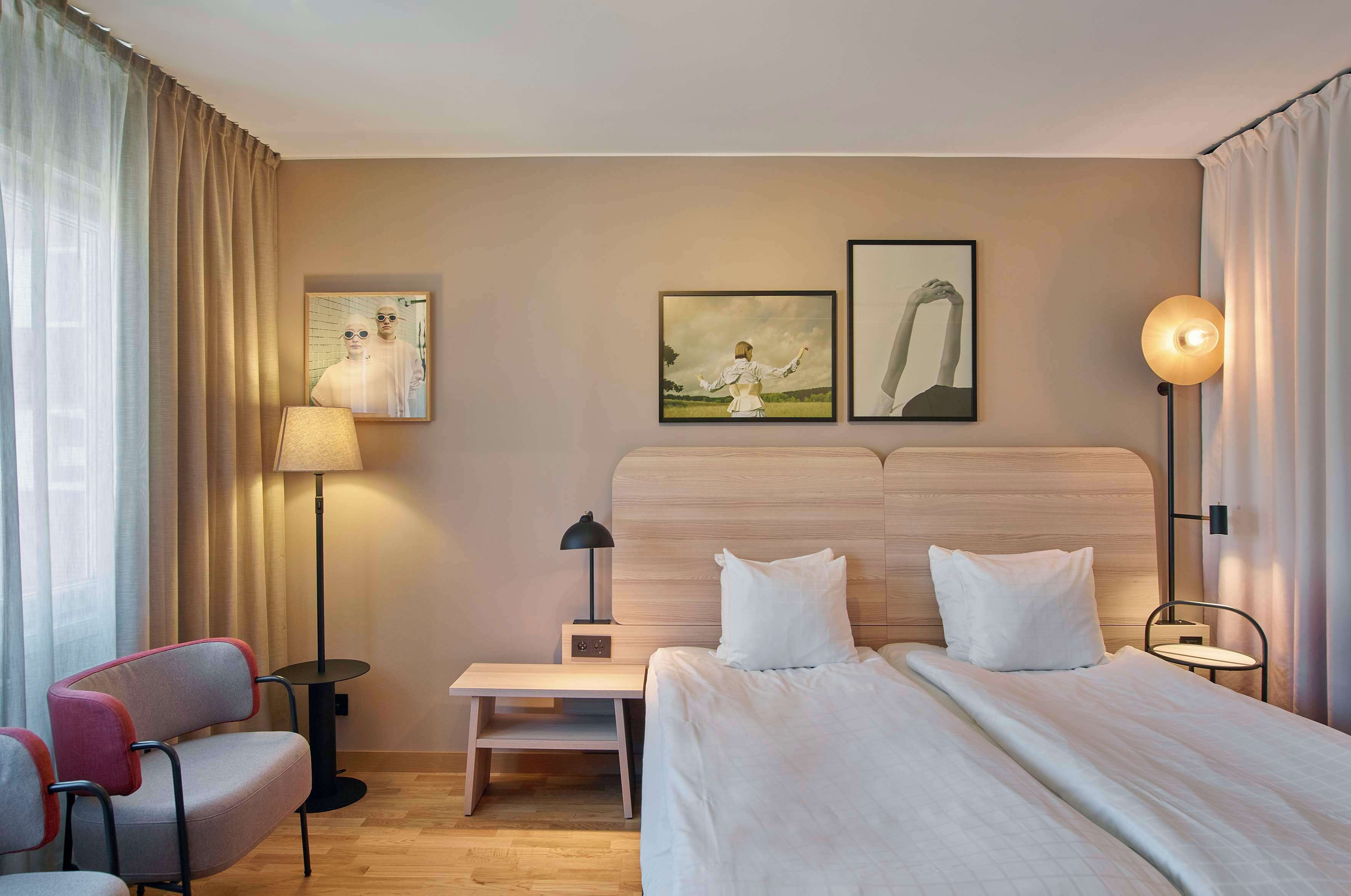 Une chambre d’hôtel avec un lit, un bureau, une chaise, une lampe et deux tableaux encadrés au mur.