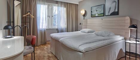 Una habitación de hotel moderna con una cama grande, un escritorio, una silla, un armario y una ventana con cortinas.