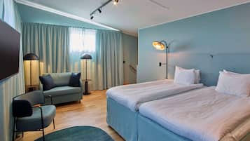 A hotel room with a bed, a chair, a desk, a lamp, and a window with curtains.