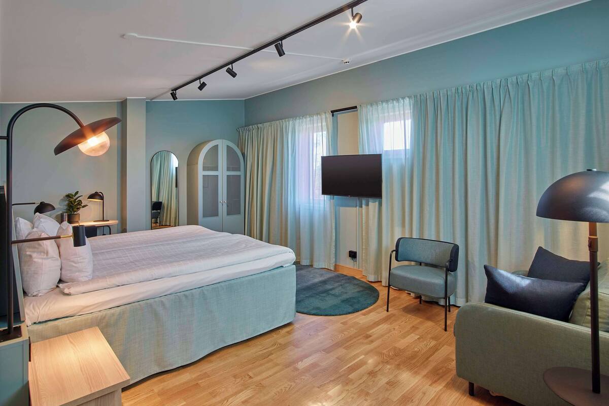 Un dormitorio moderno con una cama grande, un televisor y una zona de estar con una silla y un sofá.