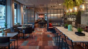A modern restaurant with a long communal table, several seating areas, and a bar.