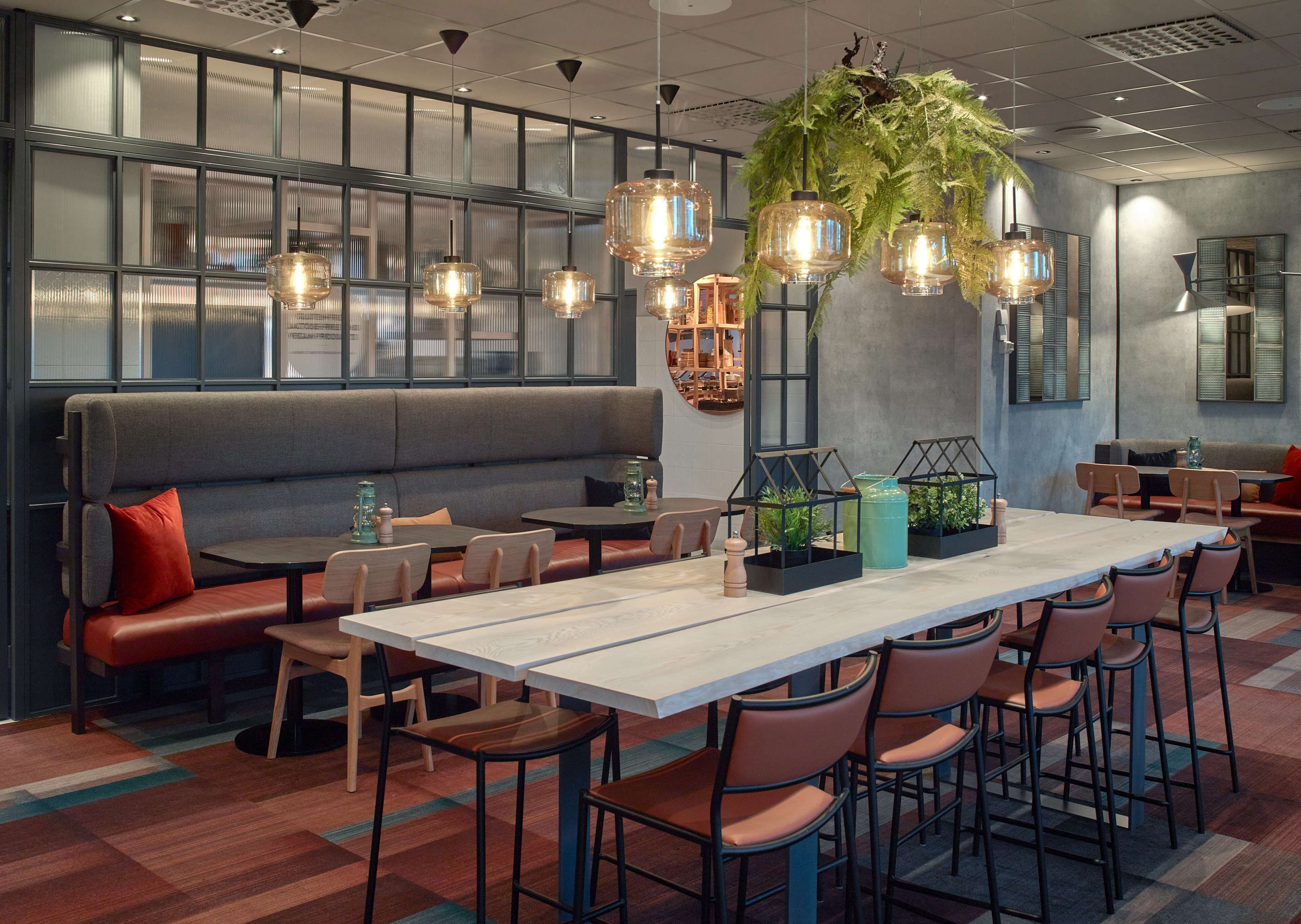 A modern restaurant interior with a long communal table, booths, and hanging pendant lights.