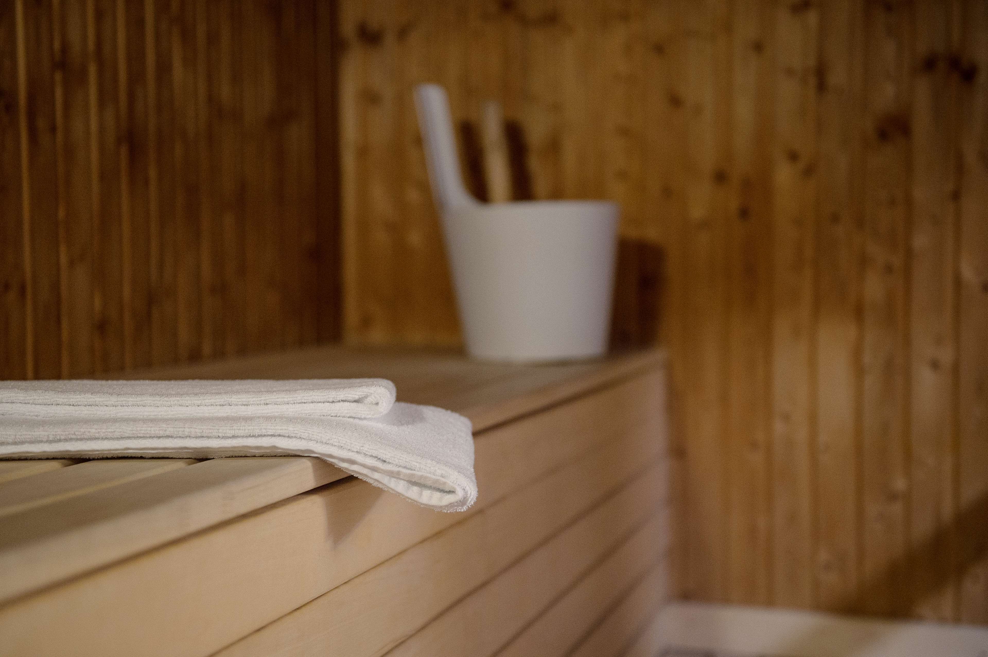 A wooden bench with a folded towel and a white cup with a spoon in a wooden cabin.