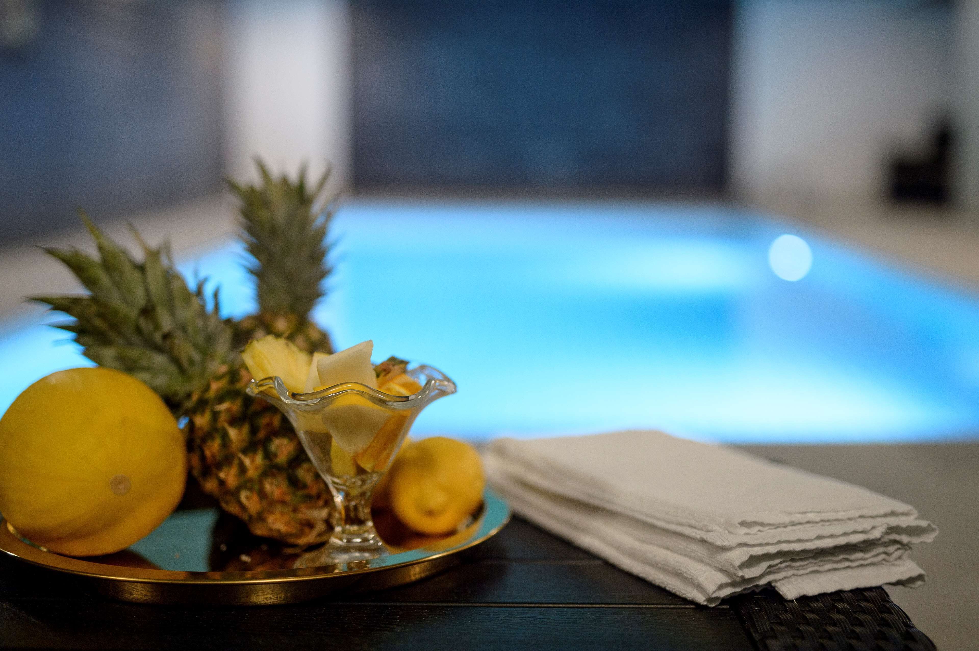 A tray with a pineapple, lemon, and a glass container with a yellow substance, possibly a drink, on a table with a blue-lit background.