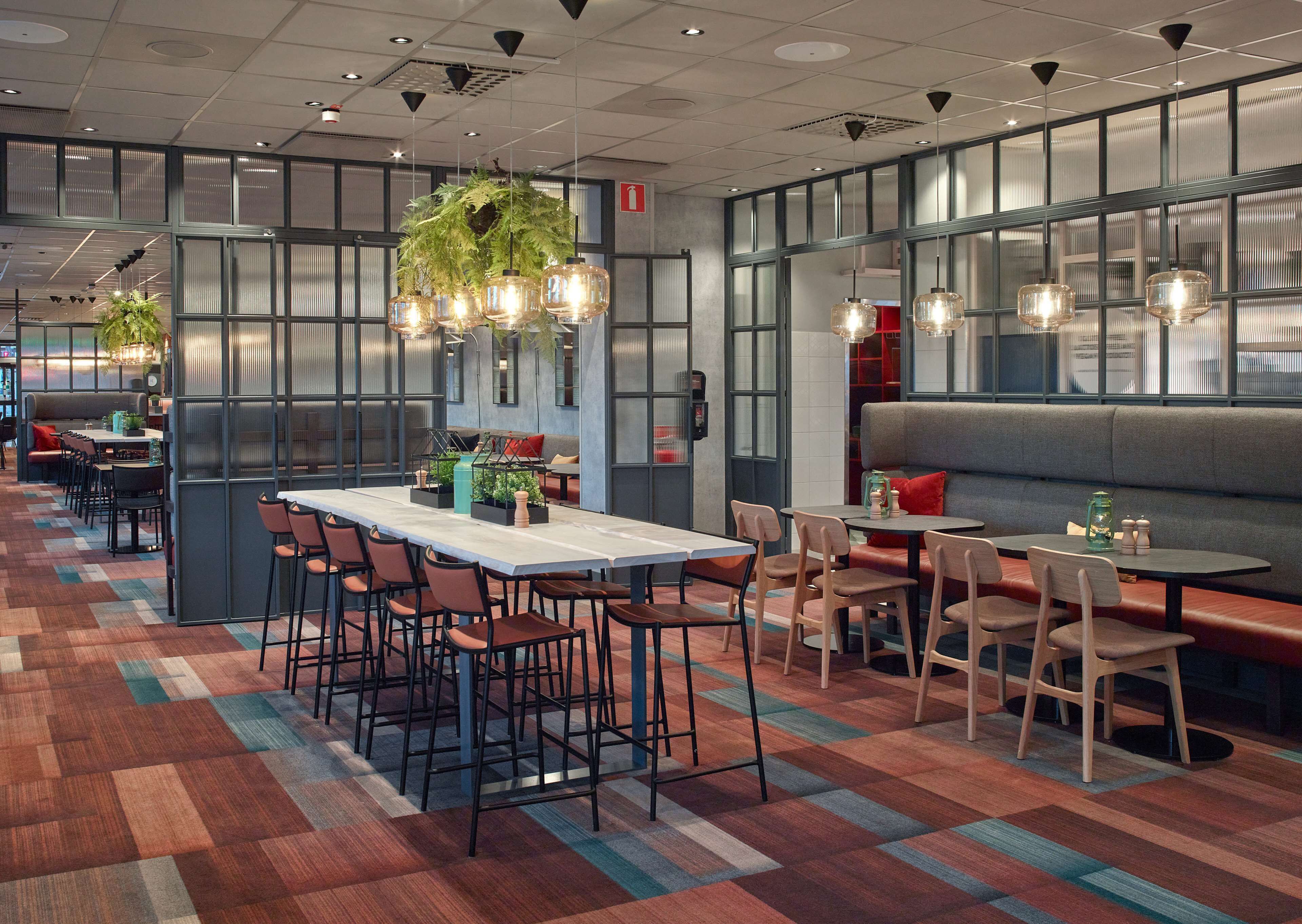 Un restaurante moderno con una mesa común larga, cabinas y mesas individuales.