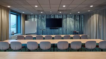 A conference room with a long table, chairs, a large screen, and a forest-themed wall.