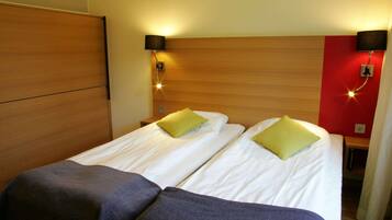 Una cama doble con ropa de cama blanca y dos almohadas verdes, un cabecero de madera y dos lámparas fijadas a la pared.