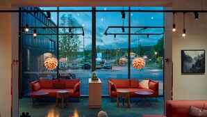 A modern interior with red sofas, a coffee table with a fire feature, and large windows offering a view of a parking lot and trees. - Scandic Örnsköldsvik (Ornskoldsvik)