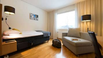 A hotel room with a bed, a sofa, a desk, and a lamp.