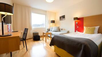 A hotel room with a bed, desk, chair, and a window with curtains.