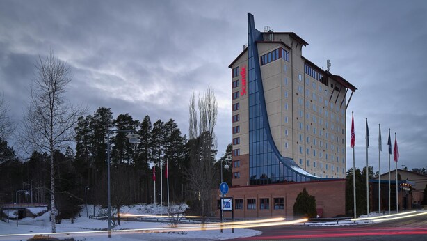 A tall hotel with a unique curved facade, a bike parking sign, and a pedestrian crossing.