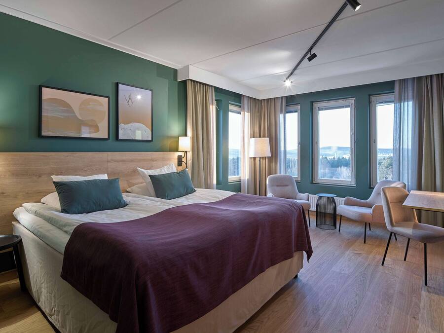 A hotel room with a large bed, two bedside tables, a desk with a chair, and a TV.