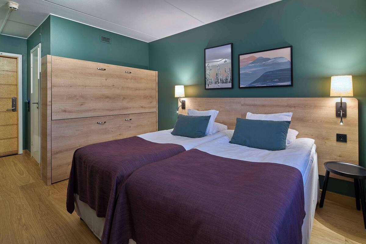 Hotellihuone, jossa on kaksi sänkyä, vaatekaappi ja taideteoksia seinillä.