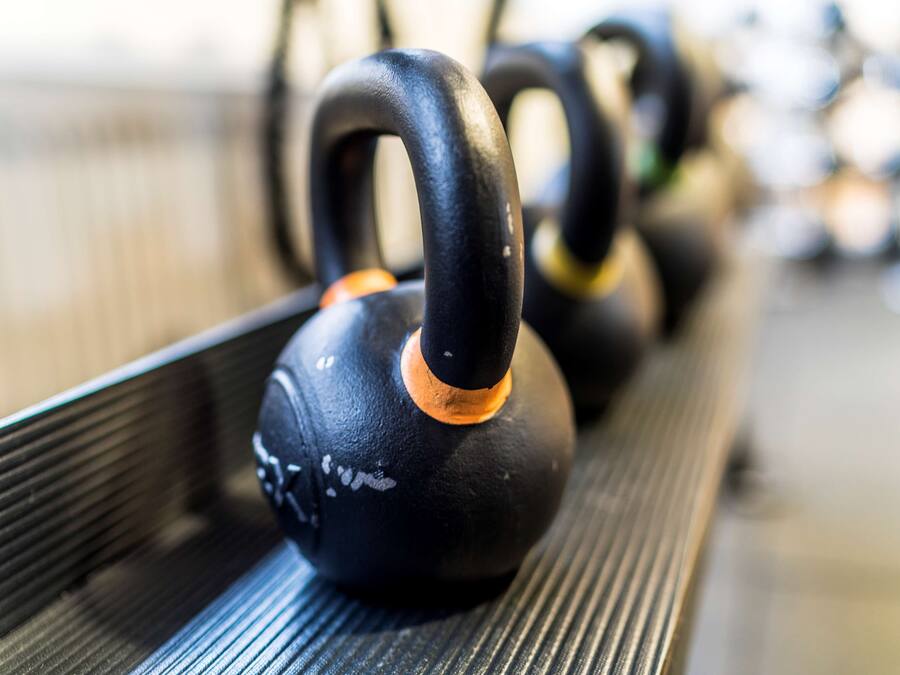 A row of black kettlebells with orange accents on a rack.