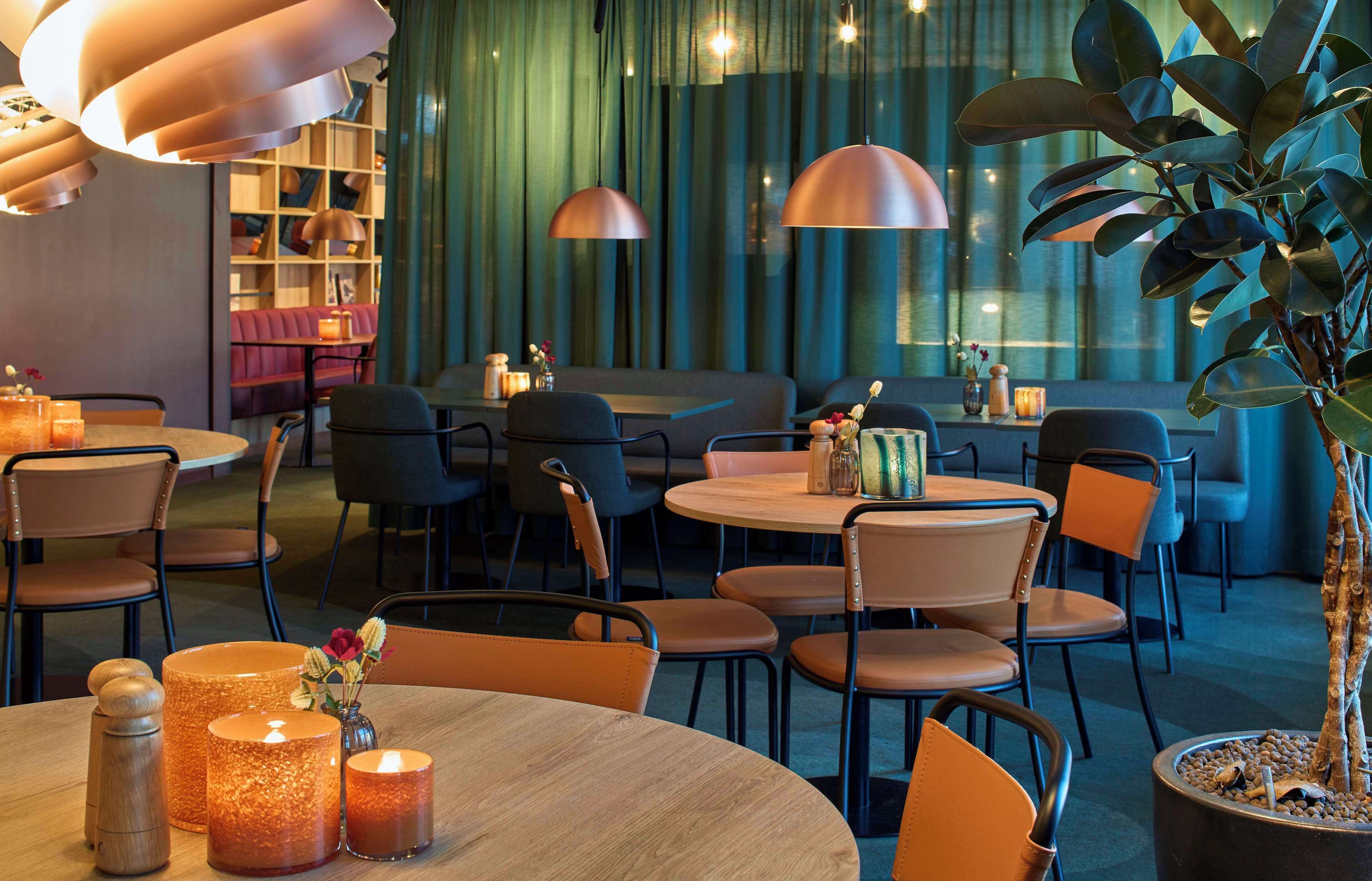 A modern restaurant with round tables and chairs, ambient lighting, and a green curtain backdrop.
