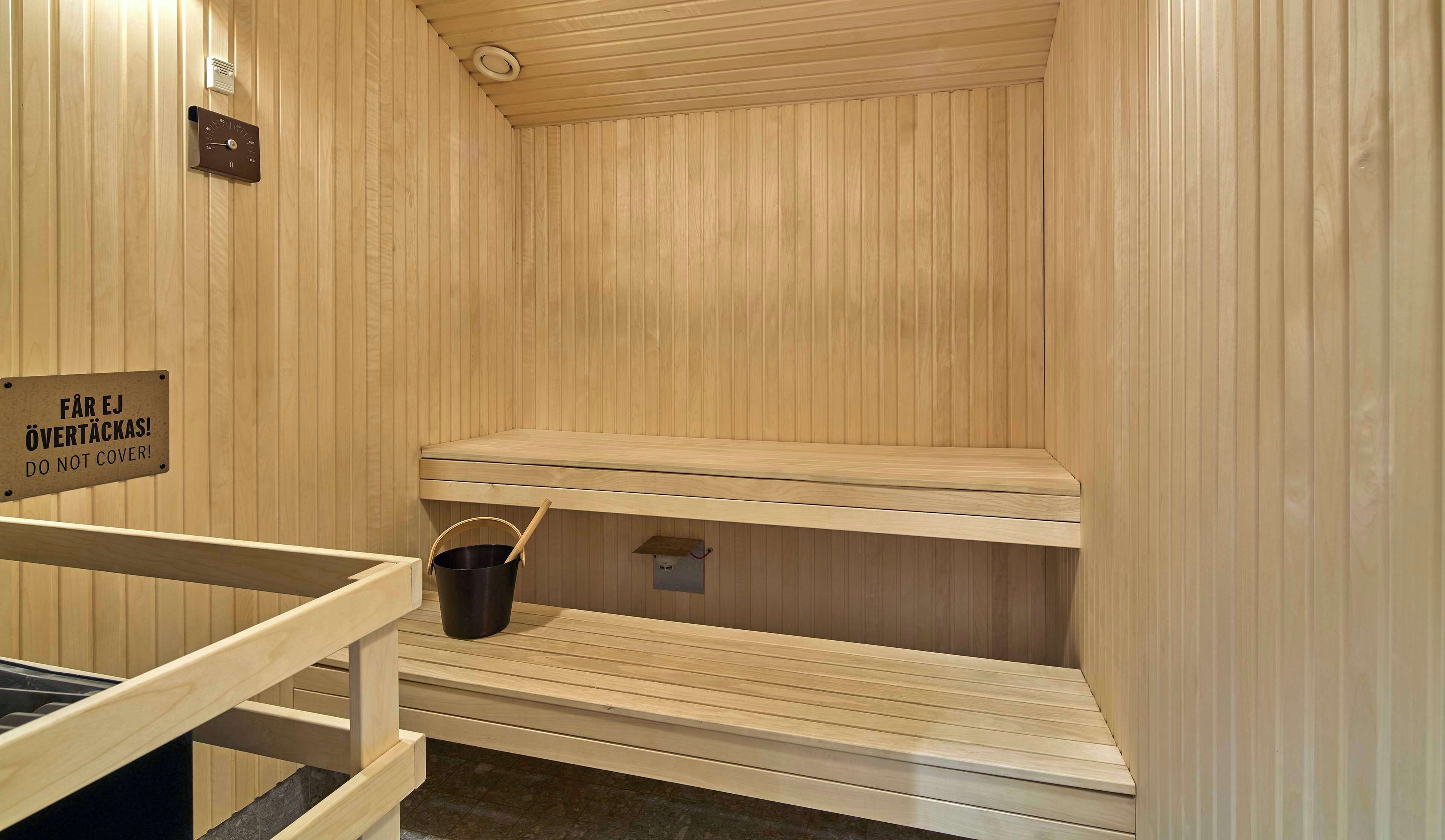A sauna with wooden benches, a bucket, and a sign instructing not to cover the benches.