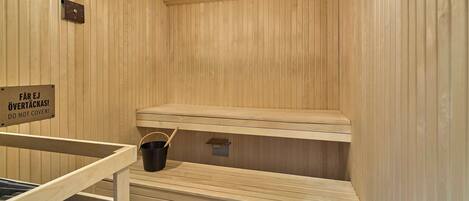 A sauna with wooden benches, a bucket, and a sign instructing not to cover the benches.