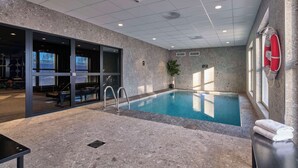 An indoor swimming pool with a stone wall, a lifebuoy, and a bench with towels.
