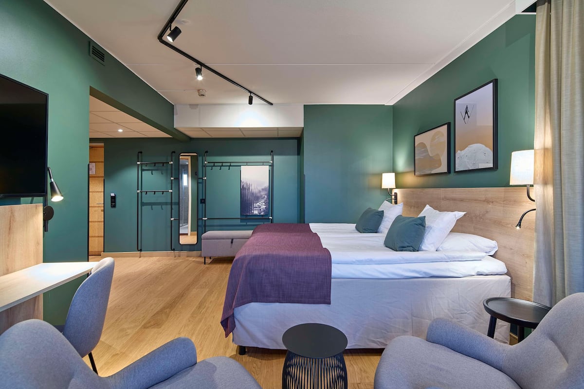 Moderni hotellihuone, jossa on sänky, oleskelualue ja televisio.