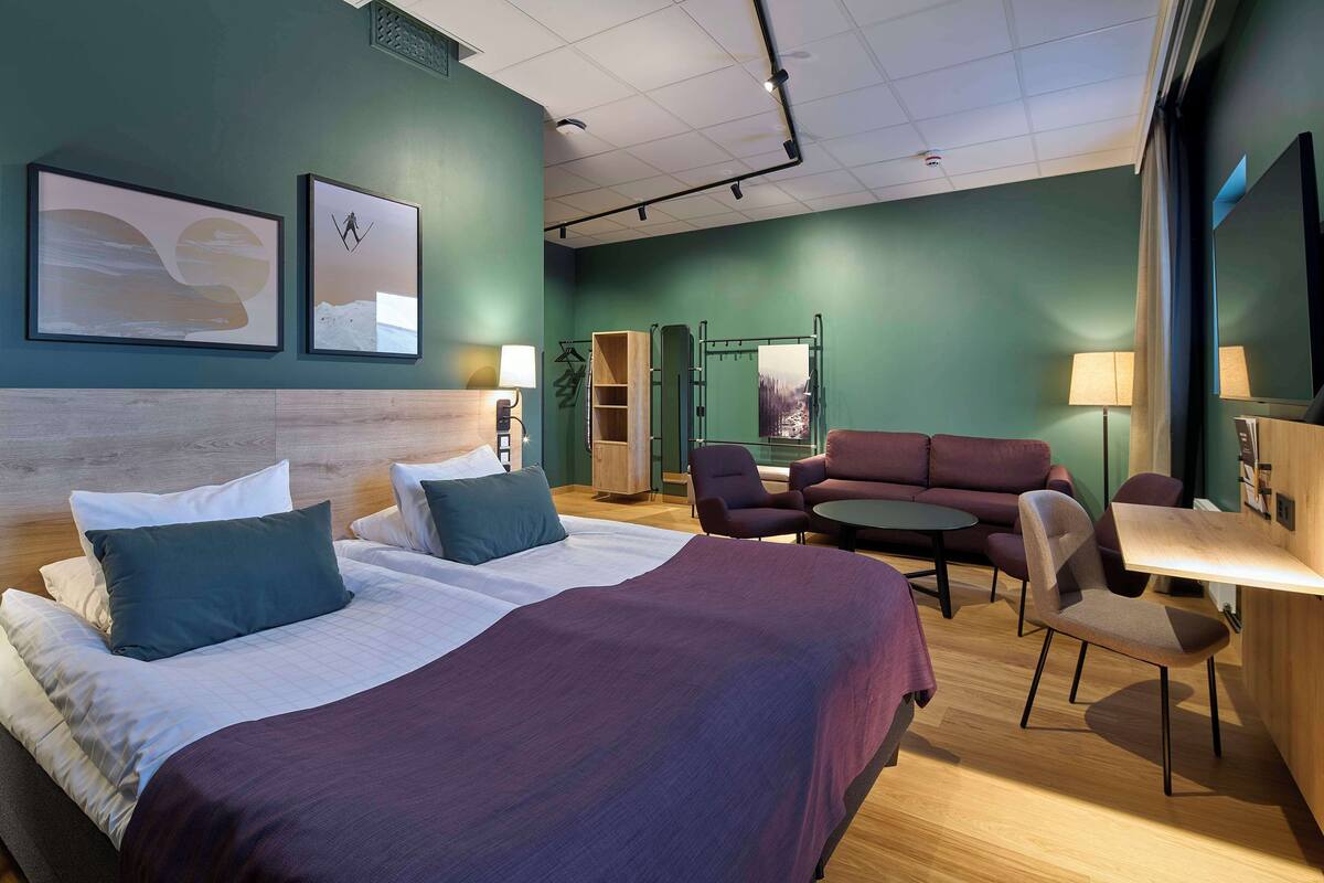 Hotellihuone, jossa on suuri sänky, kaksi nojatuolia, pieni pöytä ja sohva.