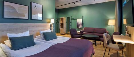 Una habitación de hotel con una cama grande, dos sillones, una mesita y un sofá.