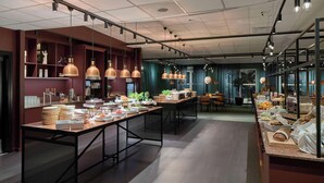 A modern dining area with long tables, pendant lighting, and a buffet setup.
