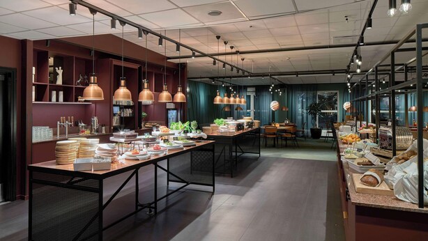 A modern dining area with long tables, pendant lighting, and a buffet setup.