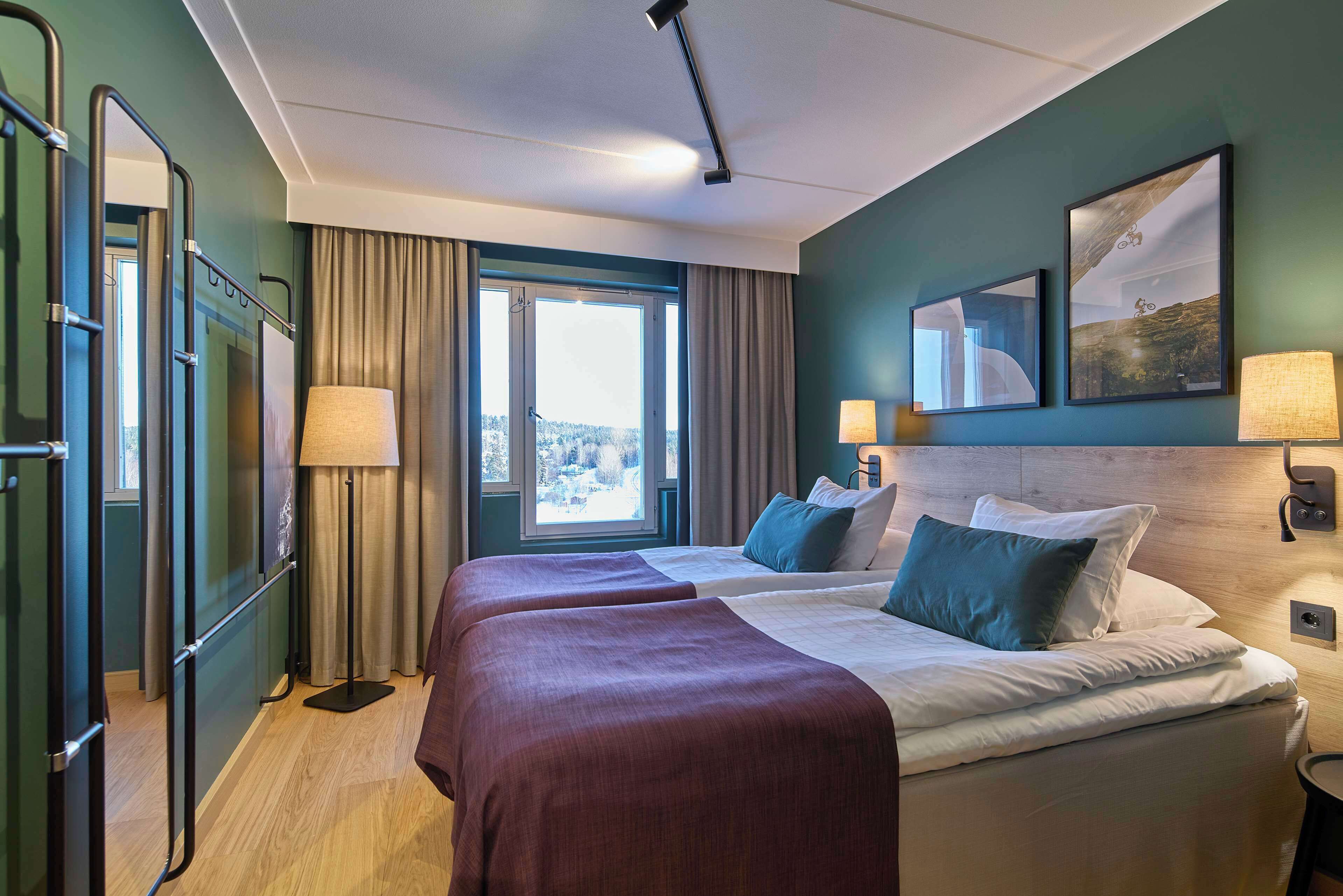 A hotel room with two beds, a large window, a view of the outdoors, and a painting on the wall.