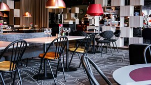 A modern restaurant interior with tables, chairs, pendant lighting, and a bar area. - Scandic Västerås (Vasteras)