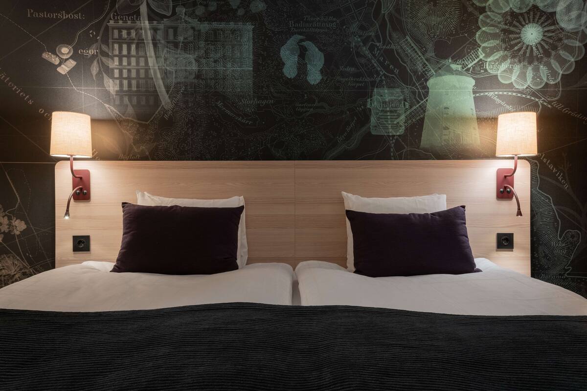 A double bed with two nightstands, each with a lamp, set against a wall with a map and decorative elements.