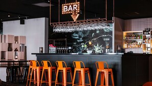 A bar area with orange bar stools, a bar counter with a wine cooler, and a wall with a map and bar sign. - Scandic Västerås (Vasteras)