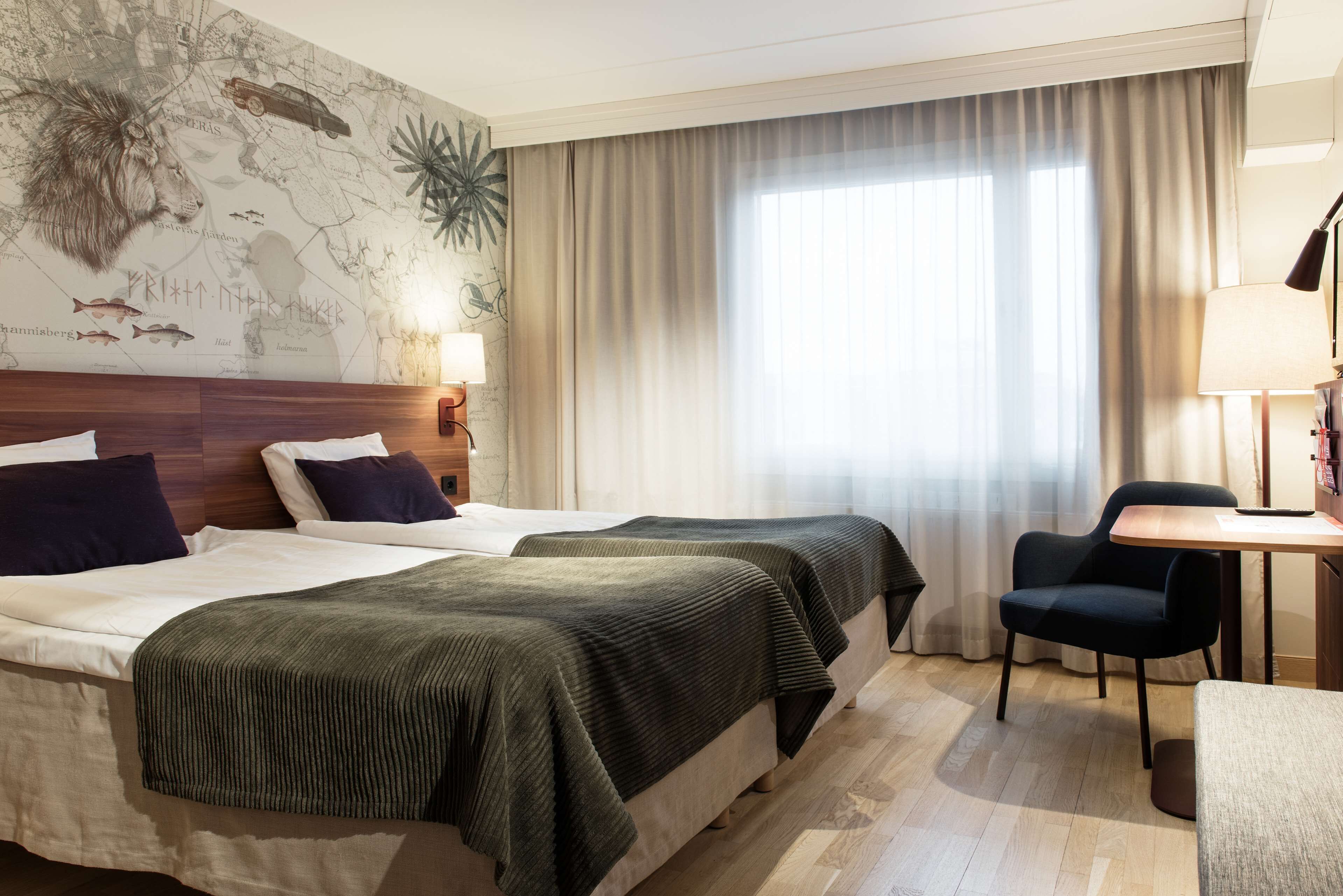 Habitación de hotel con dos camas, un mapa en la pared, un escritorio y una silla.