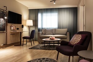 A modern living room with a sofa, armchairs, a coffee table, a TV, and a desk with a lamp.