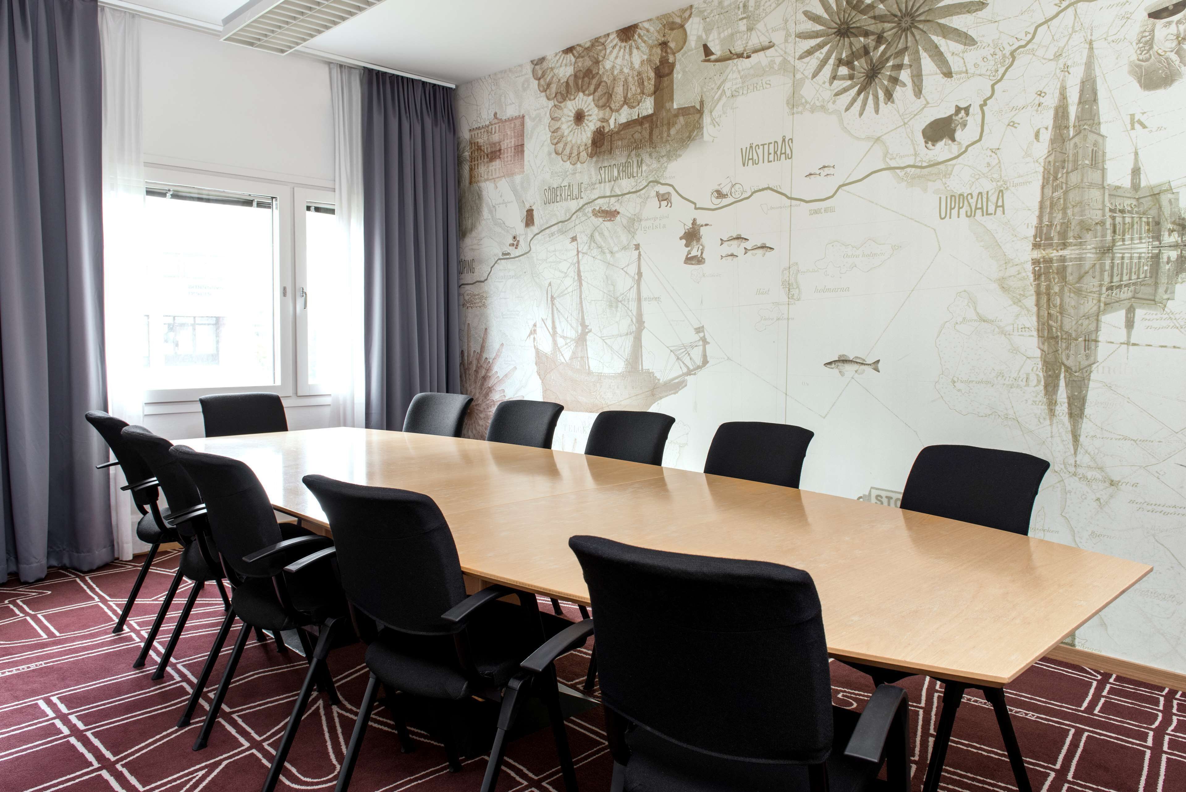 Ett konferensrum med ett stort bord, svarta stolar, en väggmålning som föreställer en karta och ett fönster med gardiner.