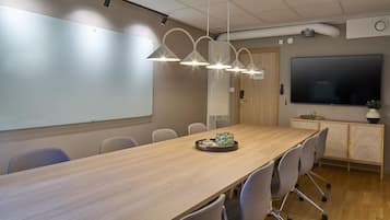 A conference room with a long table, chairs, a whiteboard, a TV, and pendant lights.