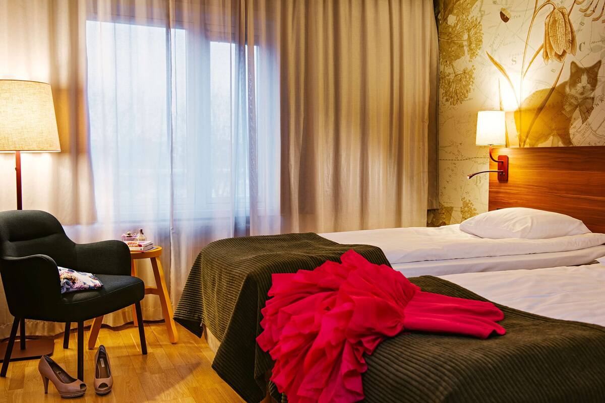 A hotel room with two beds, a chair, a lamp, and a map on the wall.
