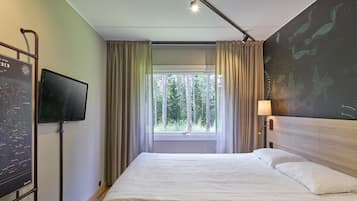 Una habitación de hotel con cama, televisor, ventana con cortinas y una pared con un mapa.