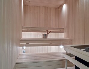 Una sauna con bancos de madera y un cubo de metal con ramitas.