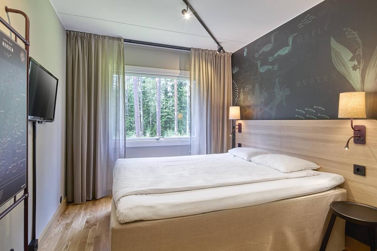 A hotel room with a large bed, a TV, a window with curtains, and a wall with a map.