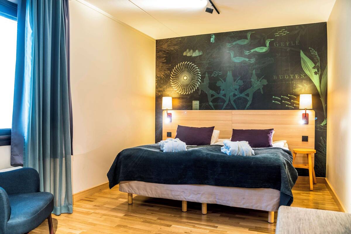 A modern hotel room with a large bed, wooden headboard, and a wall mural.